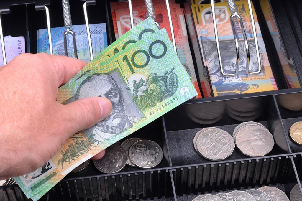 Cash flow management small business course - Photo of an open cash register with a hand inserting two $100 notes in Australian dollars